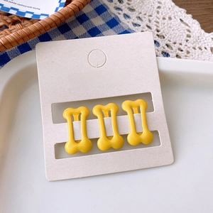 Three bright yellow bone-shaped hair clips displayed on a card for women's styling