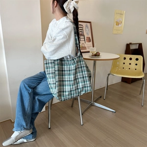 Detail of a large green plaid canvas tote bag worn on shoulder in a cafe setting