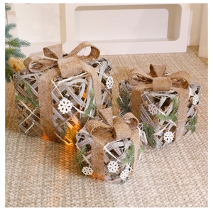 Close-up of three lighted rattan Christmas gift boxes with burlap bows and pine needles