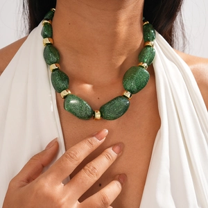 Detailed view of green acrylic irregular beads with gold rings on model's neckline