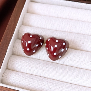 Macro shot of dark red heart earrings with white polka dots in a beige velvet jewelry box