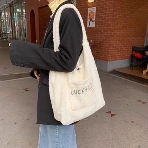 Detail of white plush fleece tote bag featuring green Lucky embroidery and orange smiley face
