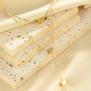 Macro shot of minimalist gold necklace with geometric cube pendants on stone