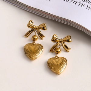 Detail of gold bow heart earrings with embossed patterns on a white background
