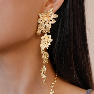 Detailed view of long gold tassel floral earrings with leaf charms worn by a model