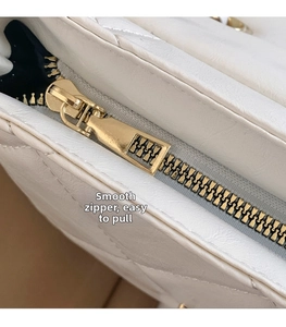 Detail of a smooth golden zipper and quilted white leather texture on a crossbody bag