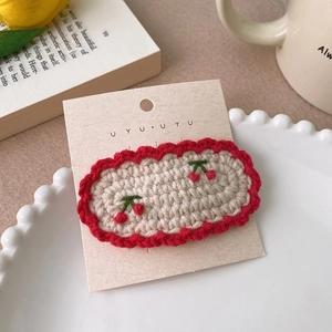 Détail d'une pince à cheveux au crochet avec broderie cerise et bordure festonnée