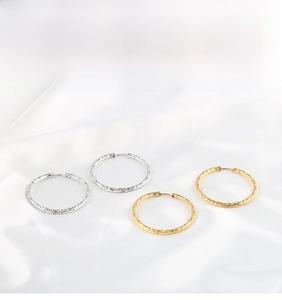 Detailed view of gold and silver hoop earrings with hammered metal texture on white silk