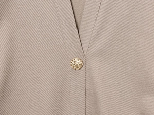 Detail eines khakifarbenes Twillkleid mit V-Ausschnitt und goldenem Zierknopf Verschluss