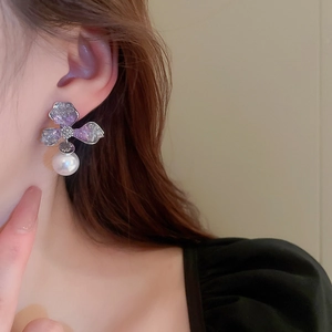 Detailed macro view of asymmetric crystal flower earrings with white hanging pearl
