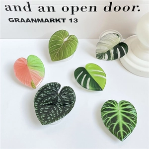 Variety of realistic acrylic leaf phone grips in green and pink colors displayed on a desk