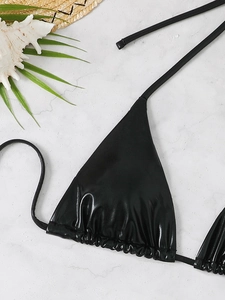 Macro shot of black glossy bikini top with thin ties on a white marble background