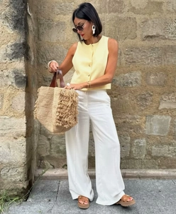 Close-up of yellow sleeveless button vest with large straw fringe tote bag and white earrings