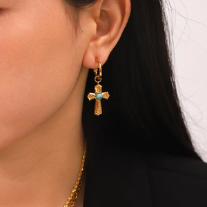 Gold hoop earrings with turquoise cross pendant worn by model on white background