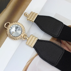 Elastic black waist belt with gold crystal buckle displayed on a fashion magazine