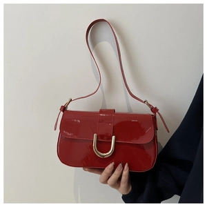 Detail of red patent leather shoulder bag featuring a gold horseshoe buckle and glossy finish