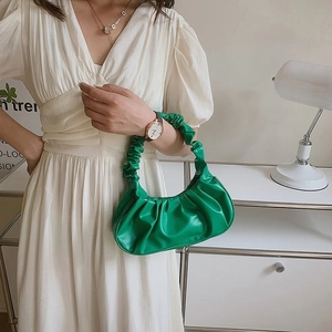 Close-up of bright green ruched cloud bag with pleated handle on a white dress model