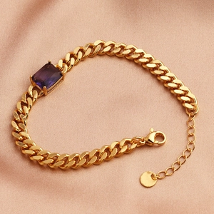 Detailed close-up of a gold-plated bracelet with a purple rectangular zircon on pink satin