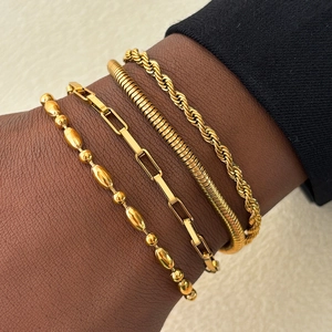 Set of four gold-plated bracelets including paperclip and snake chains on a wrist