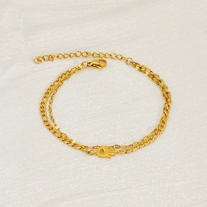 Détail d'un bracelet doré à double chaîne avec pendentif Main de Fatma sur tissu argenté