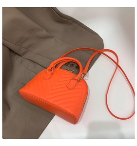 Close-up of orange shell bag featuring V-shaped stitching and slender shoulder strap