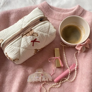 Cream teddy bear makeup bag with quilted pattern and zipper closure on pink knit background