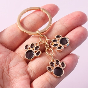 Close-up of golden metal keychain featuring three black enamel cat paw charms on pink background