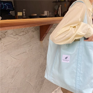 Close-up of a light blue canvas tote bag featuring an artistic feather tag and slogan