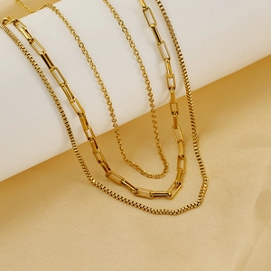 Minimalist layered gold necklace with paperclip and box chains on silk background