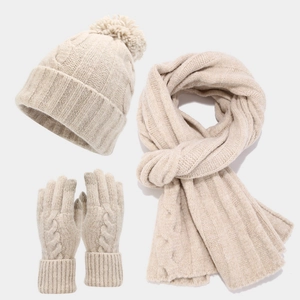 Detailed view of beige cable-knit winter set including pompom beanie, scarf, and gloves