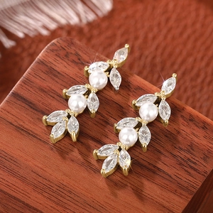 Detail van elegante gouden kwastjes oorbellen met witte parels en zirkonia bloemen