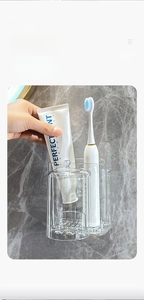 Detail showing hand placing a transparent cup on wall-mounted electric toothbrush holder