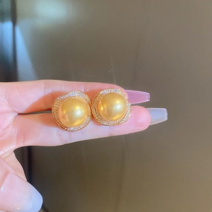 Vue macro de boucles d'oreilles perles dorées avec halo de diamants et bordure ondulée