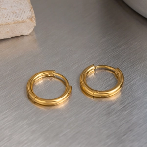 Detailed close-up of golden stainless steel hoop earrings on a textured stone background