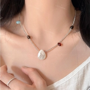 Detail showing shell pendant necklace with colorful beads and a silver rope ring on model