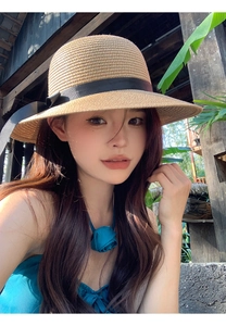 Detail of a khaki straw sun hat with black ribbon and floral necklace in sunlight