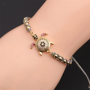 Detailed macro view of woven bracelet with zircon turtle pendant and gold beads