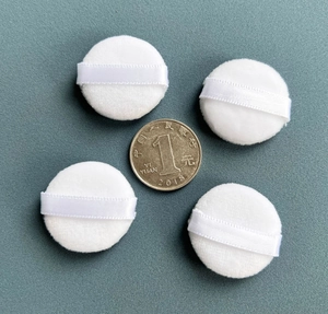 Detailed view of four small white round powder puffs compared with a coin for size