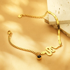 Detailed close-up of gold snake and cuban link chain bracelet with serpent charm and black gem