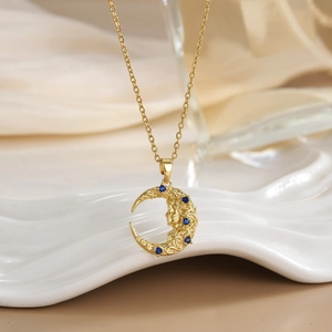 Macro view of gold-plated crescent moon pendant with face engraving and blue stones