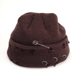 Detail of dark brown knit beanie with silver safety pin, rings and distressed holes