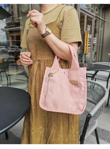 Rosafarbene Canvas-Handtasche mit Metallanhänger in einem hellen Outdoor-Café