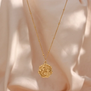 Detailed view of golden bead chain necklace featuring embossed flower and dragonfly pendant