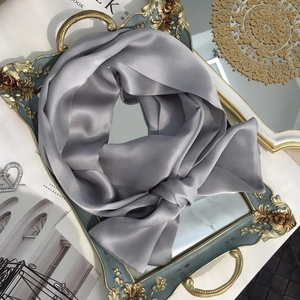 Macro detail of a grey 100% mulberry silk skinny scarf tied on a luxury mirror tray