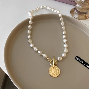 Macro detail of baroque pearl necklace with golden toggle clasp and coin pendant