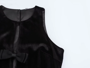 Detalle de vestido de terciopelo negro con lazo decorativo y escote redondo fino
