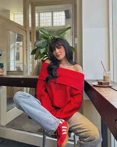 Détail du pull rouge à épaules dénudées avec un jean bleu clair dans un décor de café