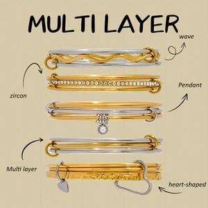 Detail of layered stainless steel bracelets with zircons, wave patterns and heart charm