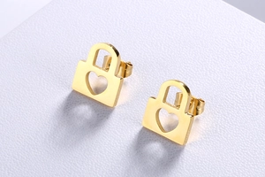 Macro shot of gold-plated heart lock earrings on white textured surface