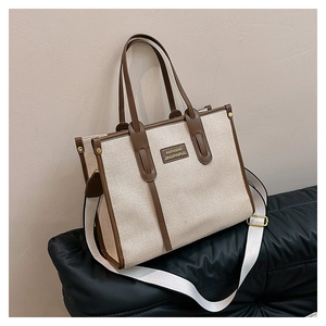 Detail of beige canvas tote bag with brown leather trim and adjustable shoulder strap